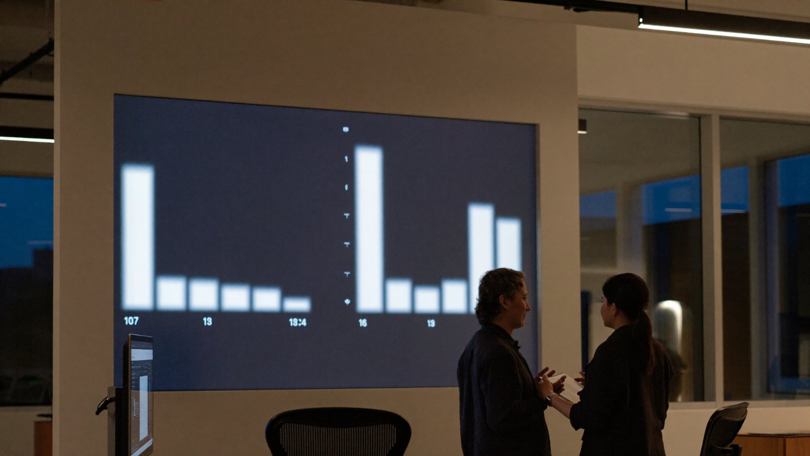 Two professionals reviewing abstract data visualizations on a large display